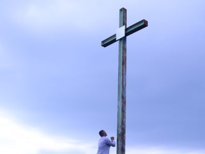 man in white shirt standing beside brown wooden cross under white clouds during daytime