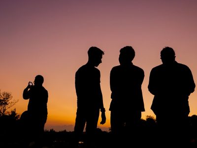 silhouette of 3 men standing on grass field during sunset
